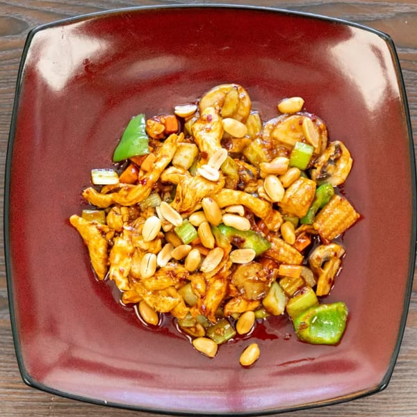 Kung Pao chicken with peanuts, green peppers, and mushrooms on a square red plate.