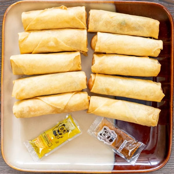A dozen golden-brown egg rolls are neatly arranged on a two-toned brown and beige plate, with mustard and duck sauce packets.