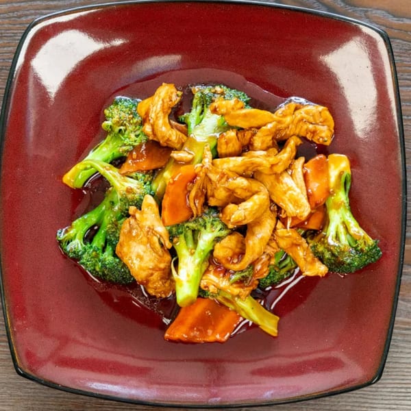 Chicken and broccoli stir-fry with carrots in a savory sauce, served on a red square plate.