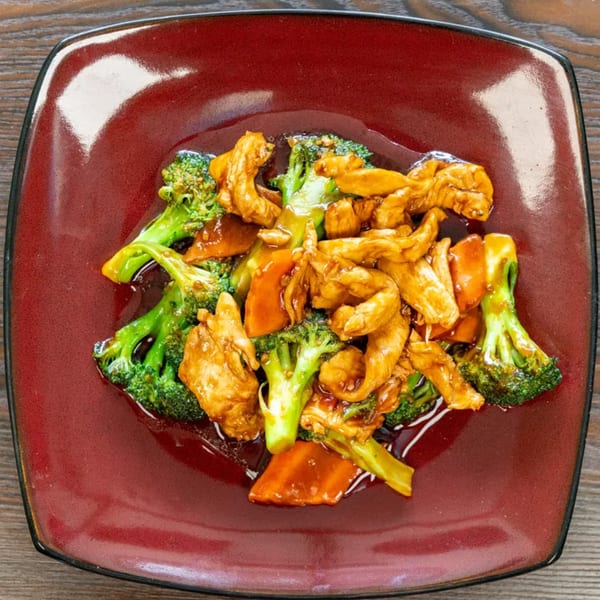 Chicken and broccoli stir-fry with carrots in a dark sauce, served on a square red plate.