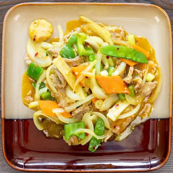 Top-down view of a square plate with beef stir-fry, onions, green peppers, and carrots.