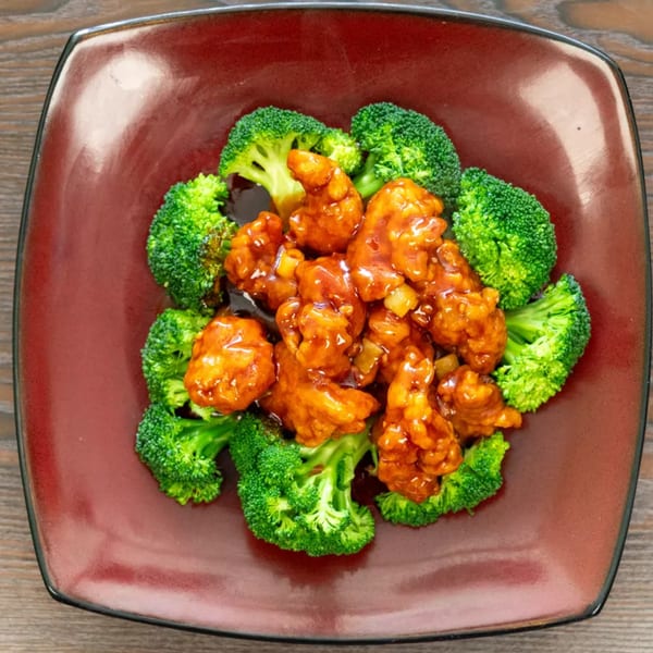 Orange chicken with broccoli florets on a square, reddish-brown plate.