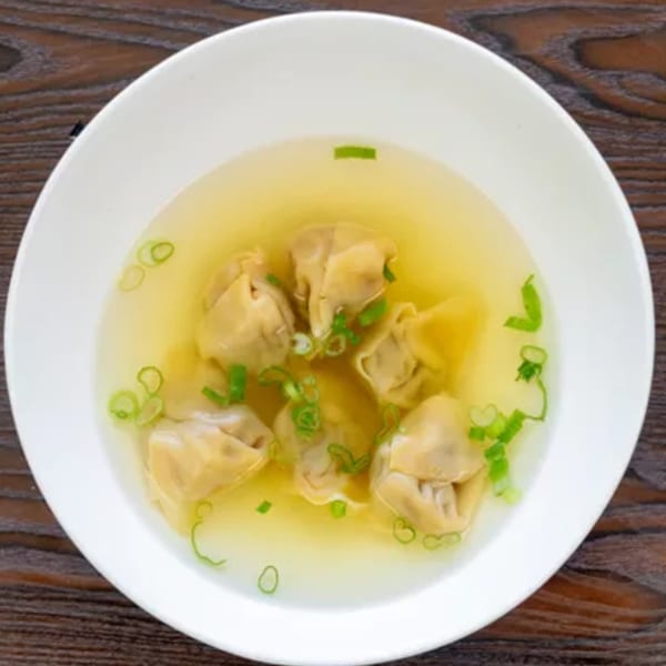 Overhead view of a white bowl filled with wonton soup, garnished with chopped green onions.